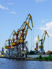 Fototapeta na wymiar Harbor pier with many cranes and stacks of bulk cargo, coal and wood chips