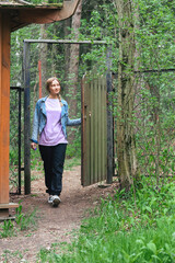 a young beautiful woman in casual clothes and sports sneakers enters the gate and closes it, a green forest remains behind the gate