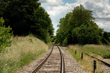 Railway in lush countryside in summer under a blue cloudy sky.