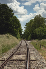 Fototapeta premium Railway in lush countryside in summer under a blue cloudy sky.