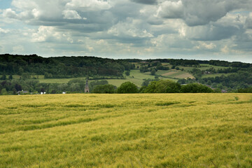 Fototapeta premium Rolling countryside with a church and some houses under a cloudy sky.