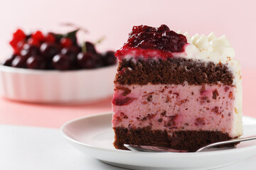 A piece of biscuit cake, with cherry soufflé with cream cheese and cherry confiture on a pink and white background. close-up