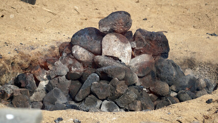 Hot coals and rocks smoldering as the imu is prepared for a luau in Hawaii. - obrazy, fototapety, plakaty