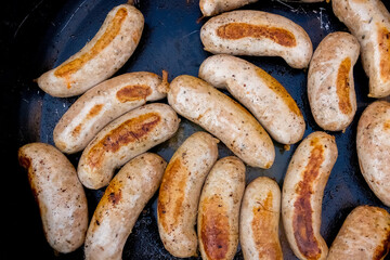 Fried juicy delicious pork sausages. View from above. Dark metal background, frying pan