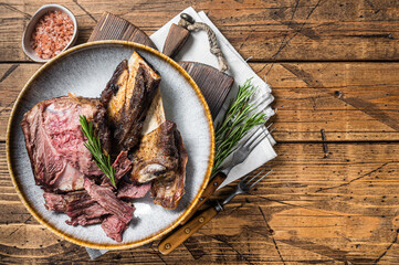 Roasted veal beef short ribs in plate with rosemary. Wooden background. Top view. Copy space