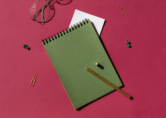 Green spiral notebook with white note paper, pen and glasses on the purple background. Copy space