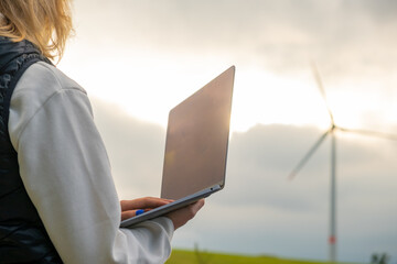 Female engineer checking the stability work of windmill with laptop in the field at sunlight. Green...
