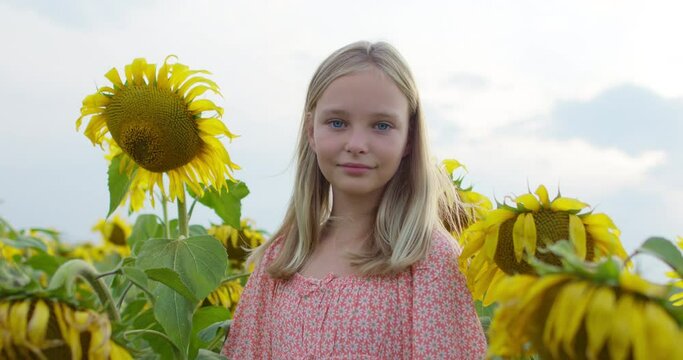 Beautiful little girl enjoying nature . Happy smiling female kid standing in sunflowers field