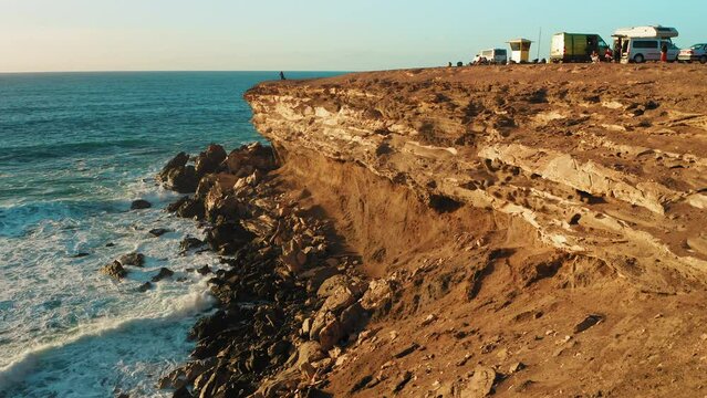 Rocky coastline alongside cliff, blue Atlantic Ocean water reflect at sunset. Nature landscape. Golden sandstone bluff beach. Tourists meet dusk. Travel destination. Fuerteventura Island, Canaries.