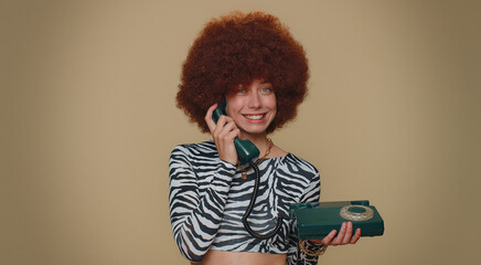 Hey you, call me back. Pretty young woman with brown lush wig talking on wired vintage telephone of...