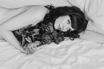 an attractive and sexy young woman with a bouquet of peonies lies in bed.