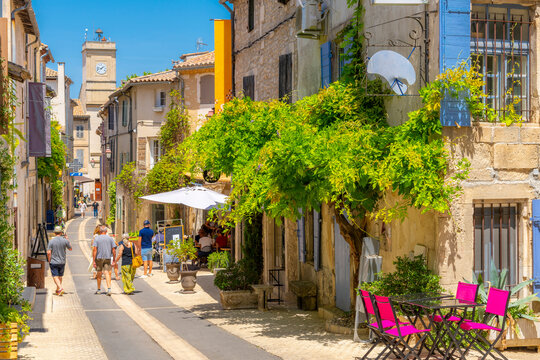 A picturesque main street through the historic medieval town of Saint-Remy de Provence, France, with the colorful shops and cafes and the clock tower in view on a summer day.