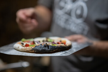 Man holding a burnt home made pizza in his hand. Pizza dough being burnt. Delicious pizza in home...