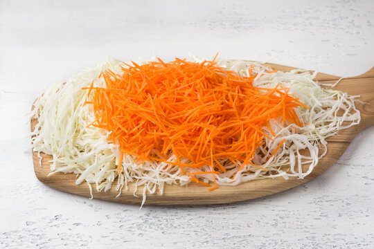 Wooden board with chopped cabbage and grated carrots on a light blue background. Preparation of Coleslow salad or other vegan food
