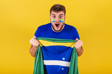Brazilian caucasian man, soccer fan from brazil, cheering in joy, holding brazil flag.