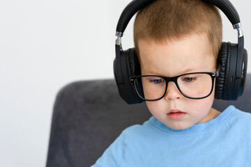 Portrait of a child in a blue T-shirt, glasses and headphones close-up.