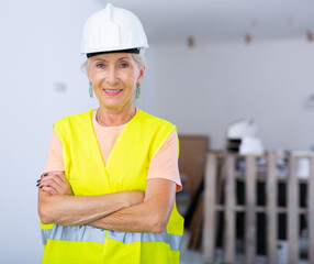 Portrait of positive builder woman in protective helmet and yellow vest in a renovated room