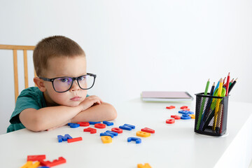 A little boy with glasses is tired and leans on his hands to rest. 