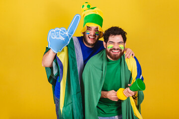 two friends, brazilians, soccer fans from brazil, using brazil flag, horn and espupa finger,...