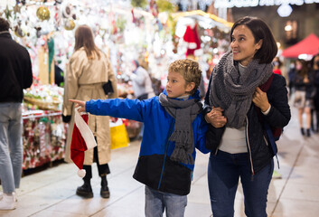 Fototapeta Portrait of happy tween boy and his loving mom walking at street fair among trade stalls offering colorful Christmas decorations obraz