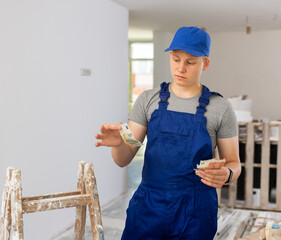 Discontented teenager boy holding bunch of money he earned by working on his first job in construction site.