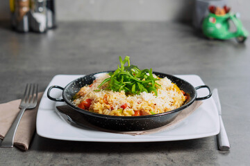 Risotto with vegetables and roasted chicken breast in the black rusticmetal pot 