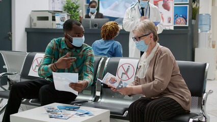 Multiethnic group of patients sitting in hospital reception to attend medical exam for covid 19 prevention. People with face mask having consultation appointment during coronavirus epidemic.