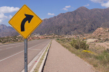 Signal indicating curve in a road in a beautiful scenery with mountains on a cloudy day.