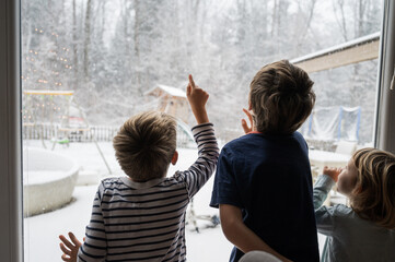 Three siblings, brothers and sister, looking out the window amazed by the snowy winter nature - 527458127