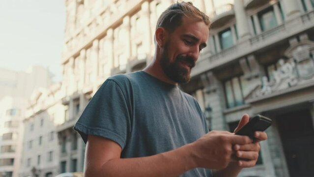 Young man with beard walks down the street using cellphone