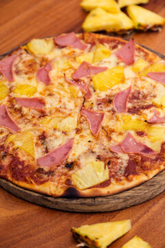 Hawaiian pizza with cheese, ham and pineapple, served on a wooden board.