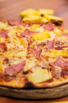 Hawaiian pizza with cheese, ham and pineapple, served on a wooden board.