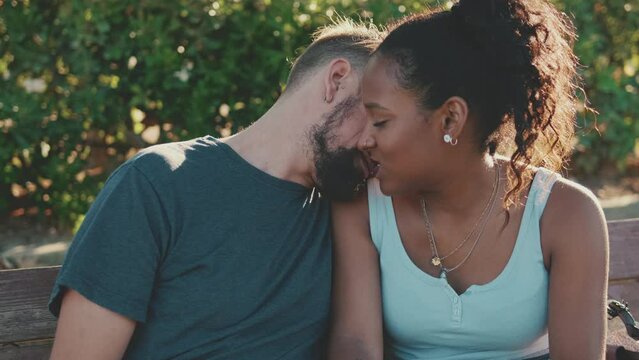 Happy smiling interracial couple kissing while sitting on bench