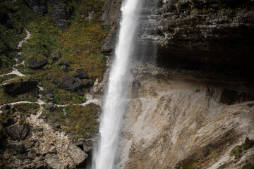 Woman Extreme Runner on A Scenic Alpine Footpath Trail Under a Big Waterfall