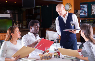 Polite waiter taking order in restaurant, helping guests in choosing meals from menu