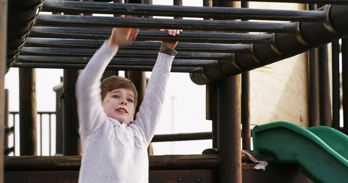 Boy climbing monkey bars on a jungle gym outdoors in a kids activity park during summer. Strong, happy and wild child having fun alone while playing on wood playground equipment in nature.