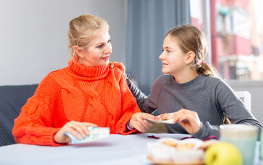 Fototapeta premium Mom gives pocket money to her daughter. Joyful daughter thanks mom