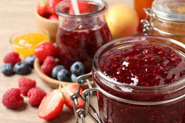 Jars with different jams and fresh fruits on table, closeup. Space for text