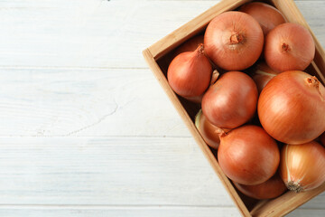 Ripe yellow onion bulbs in crate on white wooden table, top view. Space for text