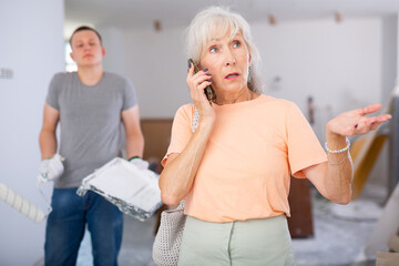 Portrait of senior woman talking on phone and making helpless gesture, disappointed by teenage boy...