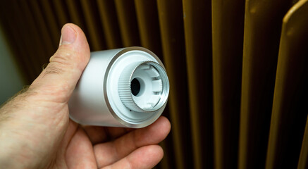 POV male hand showing modern connected radiator thermostatic head before mounting it on the red vintage radiator