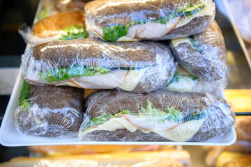 Delicious sandwiches with brown bread ham and cheese and lettuce salad wrapped in plastic protective foil - stack of delicious food ready for customers