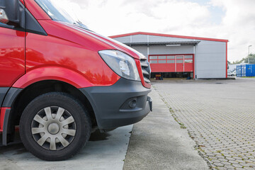 Front part of a red delivery van in front of logistics warehouse center - modern transportaiton of goods to customers