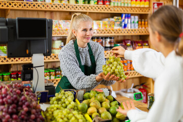 Female grocery store worker handing grape to customer after payment at checkout