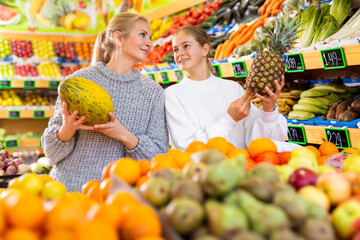 Obraz premium Smiling teenage girl choosing ripe fruits and vegetables, helping her mother to shop in supermarket..