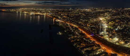 Fototapeta premium Panoramic aerial view of busy roads through coastal cityscape after sunset