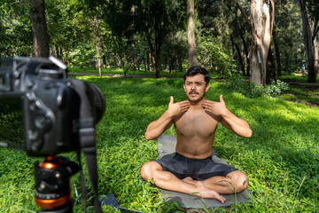 Obraz premium Young man practicing yoga asana, balance, meditating while standing on one leg on sports mat on green grass in park. Using tablet for online class.