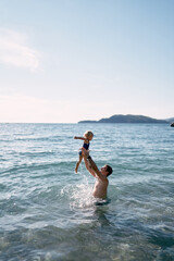 Dad throws up a little girl in his arms, standing in the sea. High quality photo