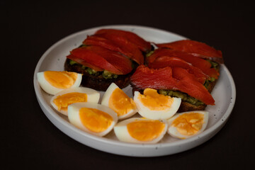 Delicious toast with salmon, boiled egg and avocado on a white plate. Healthy eating, breakfast.