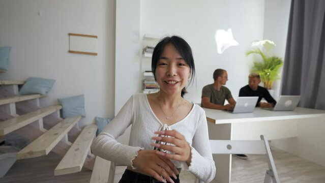 POV of joyful Asian woman coming back to conversation on video call. Young brunette sits at workplace to continue talking with friend closeup